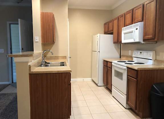 A kitchen with white appliances and wooden cabinets at Rosemary Apartments, Conroe, TX