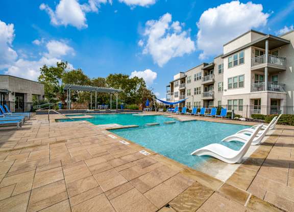 a swimming pool with chaise lounge chairs and a slide in front of an apartment building at The Landings at Brooks City-Base, Texas, 78235
