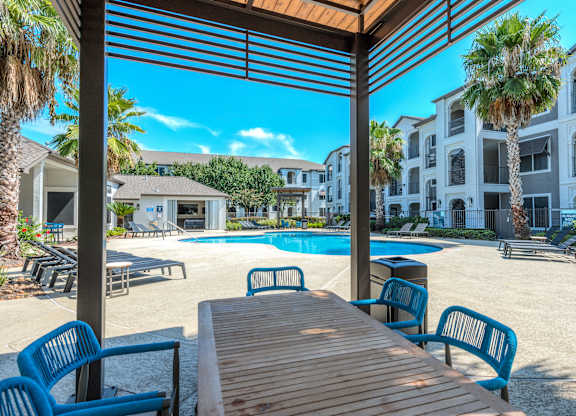 A wooden table is in the foreground of a sunny poolside area at Rosemary Apartments, Conroe, TX, 77384