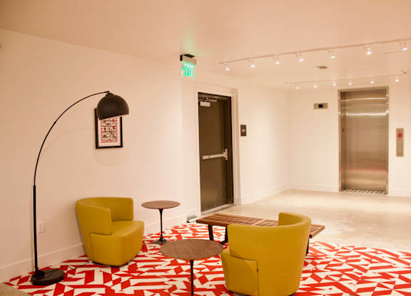 Lobby seating area with yellow chairs and floor lamp at THE'68 Apartments, San Antonio, TX 78205
