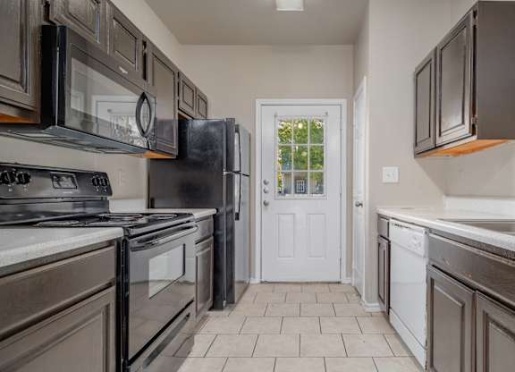 Galley kitchen with dark wood cabinets and black appliances at Houston Street Townhomes Apartments, Texas, 78220