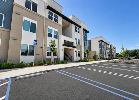 A parking lot in front of apartment buildings with a blue sign on the left.