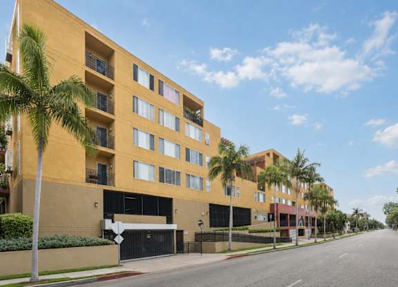 A street view of a residential area with apartment buildings and palm trees.