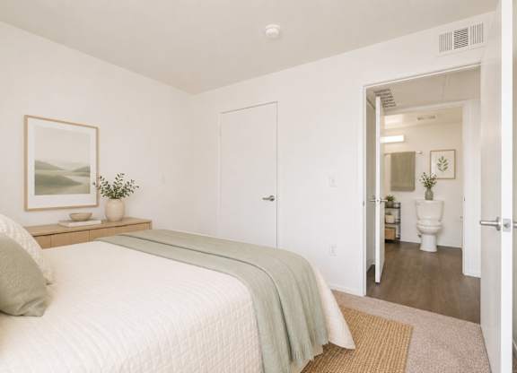 A bedroom with a bed, a nightstand with a plant, and a painting on the wall.