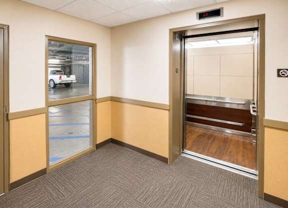 A room with a brown door and a window showing a parking lot.