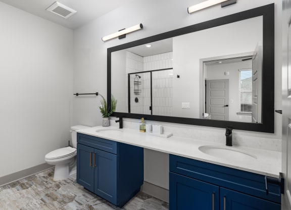 a bathroom with blue cabinets and a large mirror at Abberly Foundry Apartment Homes, Nashville