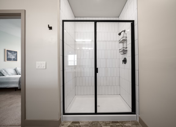 a walk in shower with white tile and a glass door at Abberly Foundry Apartment Homes, Nashville, 37203