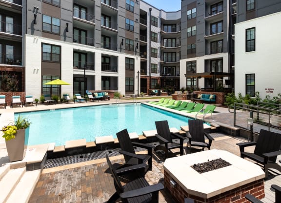 an outdoor swimming pool with lounge chairs and a fire pit in front of an apartment building at Abberly Foundry Apartment Homes, Nashville, 37203
