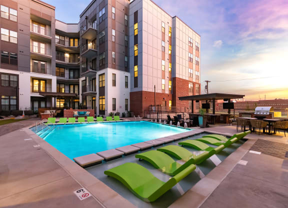 a swimming pool with green lounge chairs in front of an apartment building at Abberly Foundry Apartment Homes, Nashville, TN