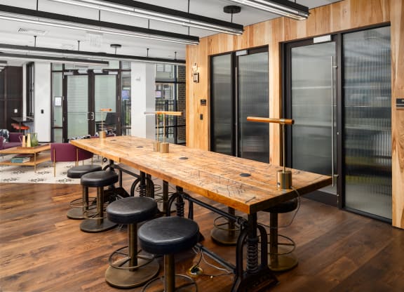 a long wooden table with black stools in a room with glass doors at Abberly Foundry Apartment Homes, Nashville, Tennessee