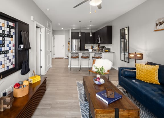 a living room with a blue couch and coffee table and a kitchen in the background  at Abberly Noda Vista Apartment Homes, North Carolina