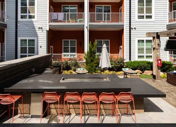 an outdoor kitchen with a bar and stools in front of an apartment building  at Abberly Noda Vista Apartment Homes, North Carolina, 28206