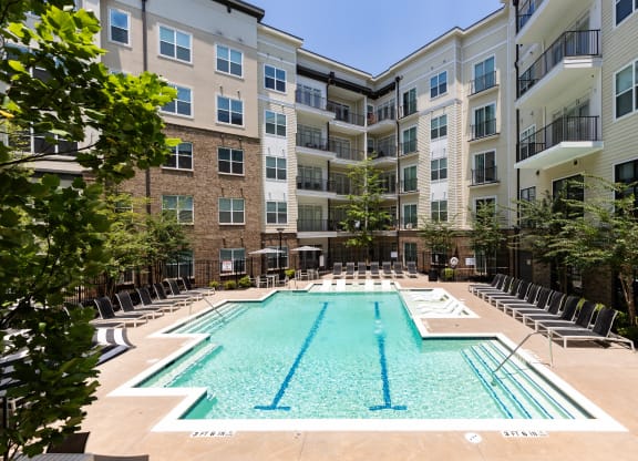 an outdoor swimming pool with chaise lounge chairs and an apartment building in the background at Abberly Onyx Apartment Homes, Decatur, Georgia