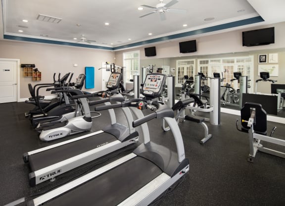 a gym with cardio equipment and televisions on the wall