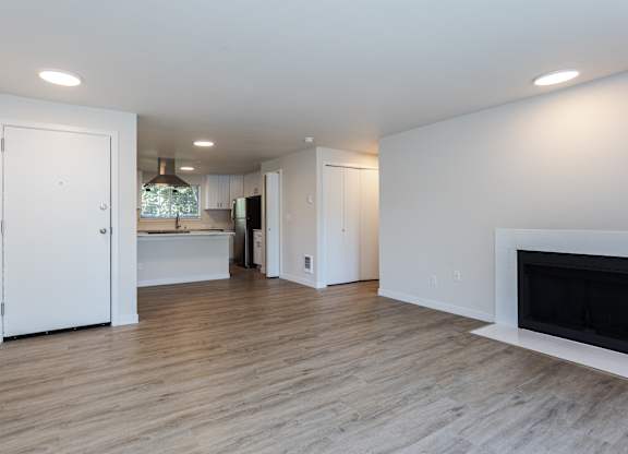 A white interior with a fireplace and a kitchen in the background.