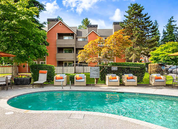 A pool surrounded by orange chairs and a building in the background.