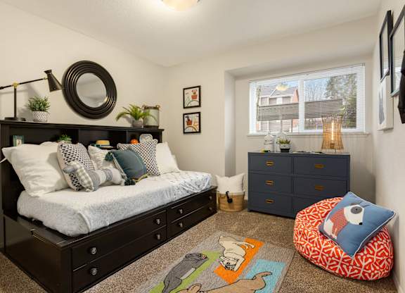 A bedroom with a bed, dresser, and a window with a view of a house.