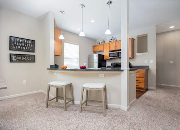 A kitchen with white walls and a white ceiling with a fridge, stove and bar stools.