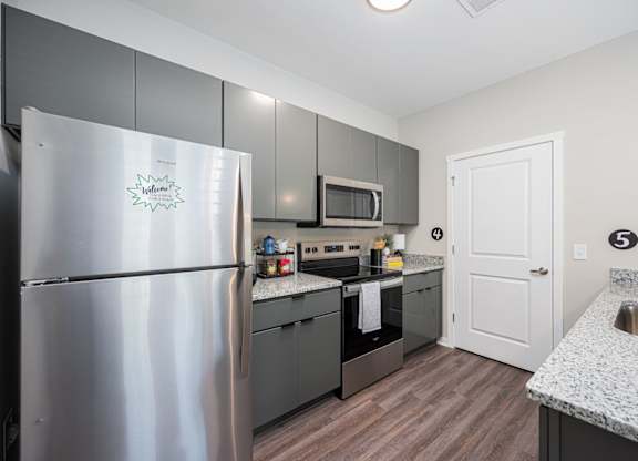 A kitchen with a refrigerator, microwave, oven, and sink.