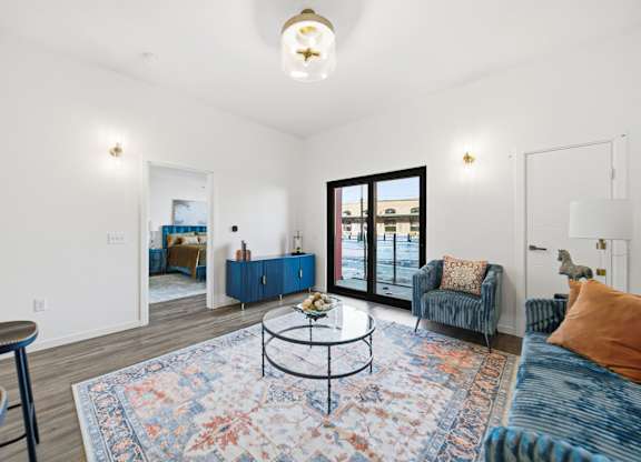 A living room with a blue rug and a glass table.