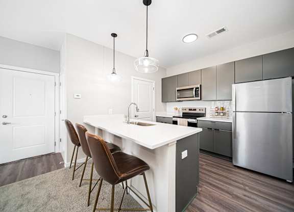 A modern kitchen with a white island and brown chairs.