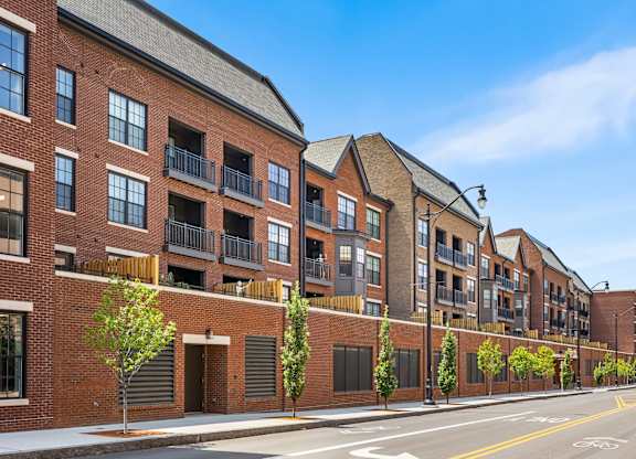 A row of red brick buildings with balconies and trees in front.