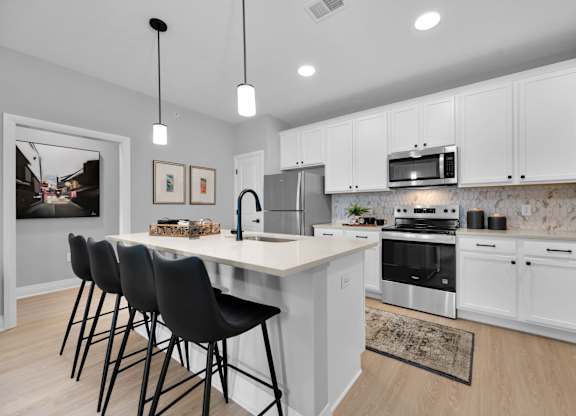 A kitchen with white cabinets and a large island with chairs.