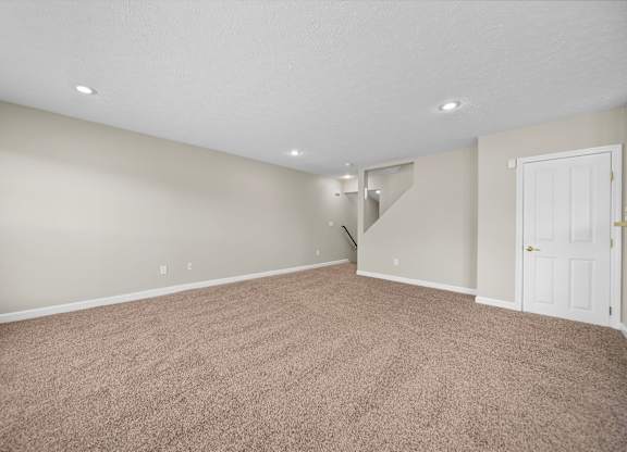 A room with a carpeted floor and a staircase in the background.