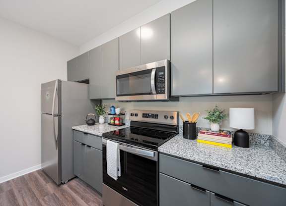 A kitchen with a refrigerator, microwave, oven, and countertop with a plant and a book on it.
