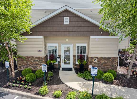 A building with a brown roof and a white door is surrounded by bushes and trees.