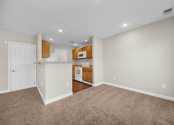 A room with a kitchenette and carpeted floor.