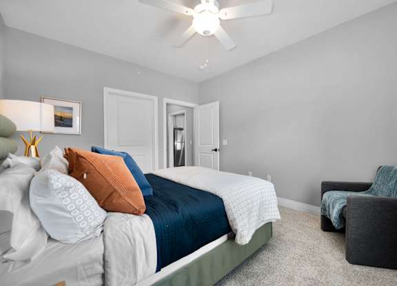 A bedroom with a bed, a chair, and a ceiling fan.
