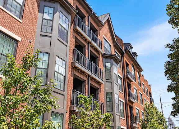 A red brick building with balconies and trees in front.