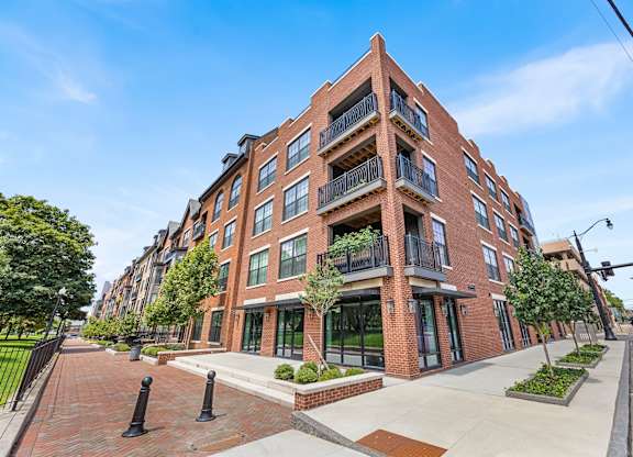 A red brick apartment building with a black fence and bushes in front.