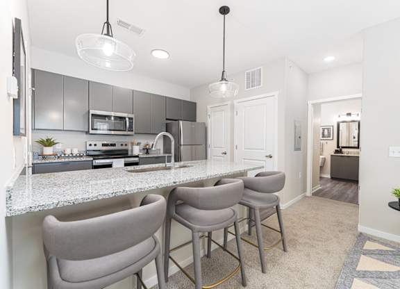 A kitchen with a bar area and grey chairs.