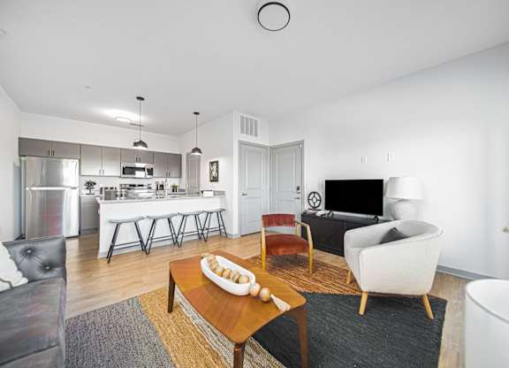 A modern living room with a white sofa, a wooden coffee table, and a kitchen area in the background.