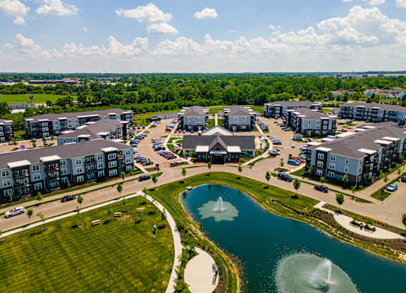 A large aerial view of a residential complex with a fountain in the middle of a pond.