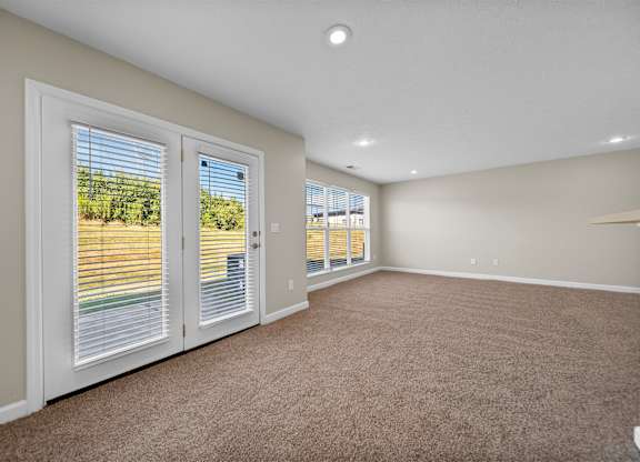 A room with carpeted floor and a view of a vineyard through the windows.