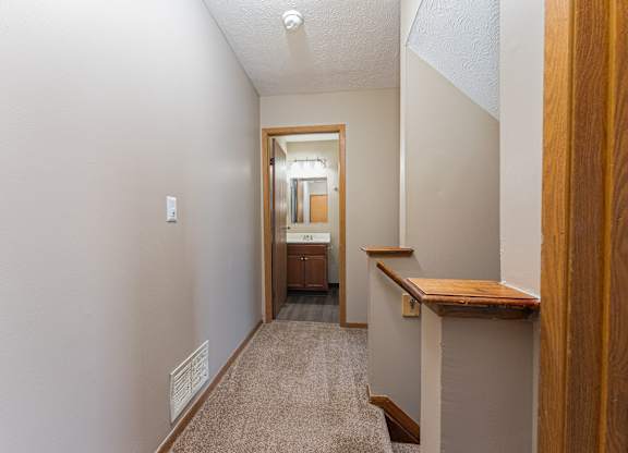 A hallway with a carpeted floor and a wooden railing on the right side.