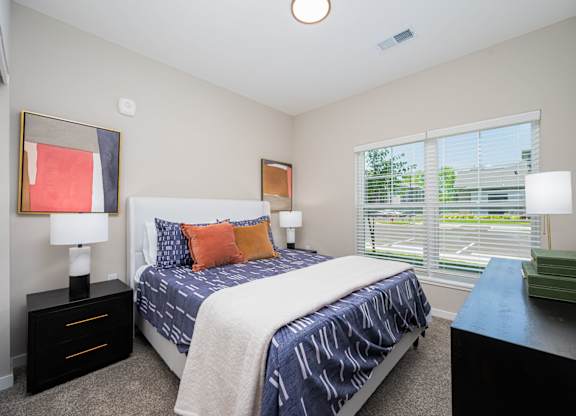A bedroom with a bed, nightstands, and a window with blinds.