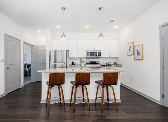 A kitchen with white cabinets and a white island with two bar stools.