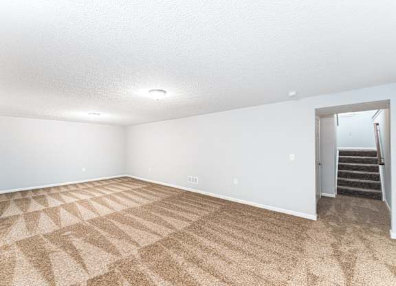 A room with a carpeted floor and a staircase in the background.