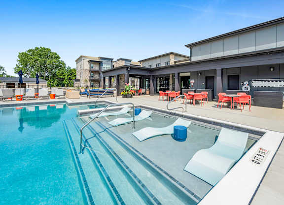 A large outdoor swimming pool with a glass barrier and red chairs.