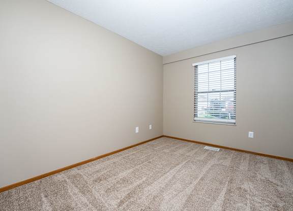 A room with a carpeted floor and a window with blinds
