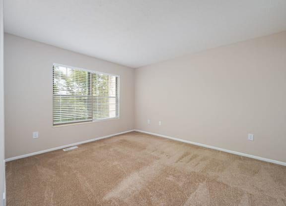 an empty living room with a window and carpeting