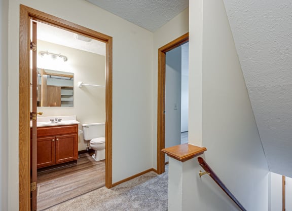 a landing leading to a bathroom with a toilet and a mirror