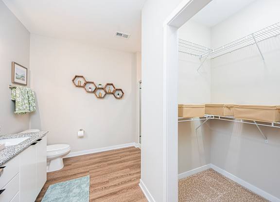 A white bathroom with a toilet, sink, and a closet with clothes hanging.