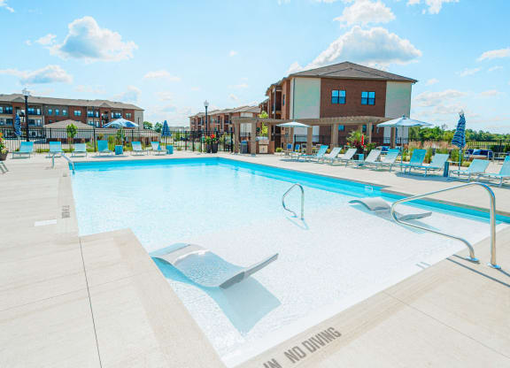 a swimming pool with chairs and a building in the background