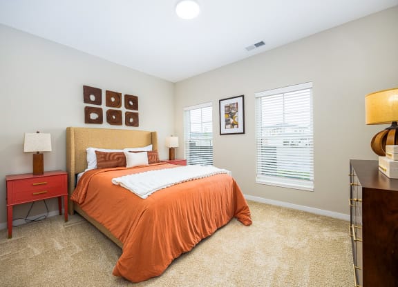 a bedroom with an orange bed and two windows