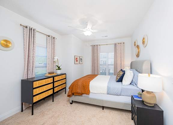 A bedroom with a bed, nightstand, and a dresser with a plant on top.
